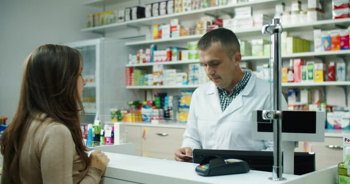 Man pharmacist in uniform sells medicines to the buyer by prescription. Against the background of a shelf with medicines. High quality 4k footage