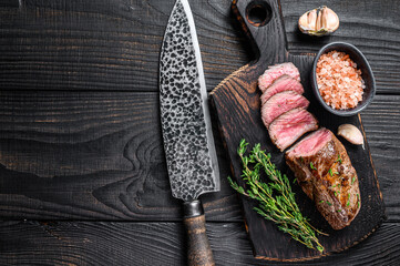 Grilled lamb tenderloin meat steak  on a meat cleaver. Black wooden background. Top view. Copy space