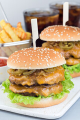 Double cheese burger with caramelized onion, lettuce and jalapeno, served with french fries and soda, on white plate, vertical