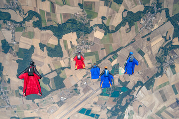 Team of wingsuit fliers glide in formation at sunset