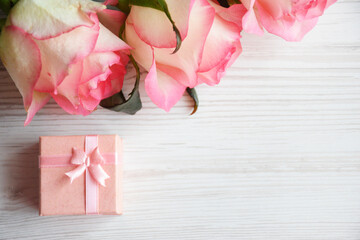 Pink gift box and tender roses on light wooden background. Valentines day concept, Flat lay.