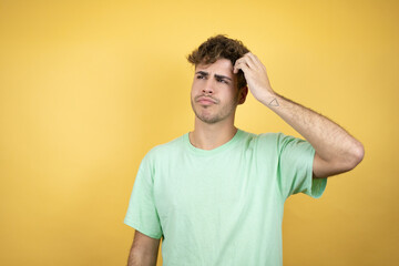 Fototapeta na wymiar Handsome man wearing a green casual t-shirt over yellow background confuse and wonder about question. Uncertain with doubt, thinking with hand on head