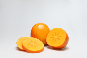 One whole staying and one half persimmon fruits with slices next to each other on white background - portrait