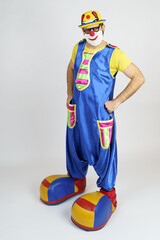 A clown in a bright blue and yellow suit, glasses and a hat is dancing.