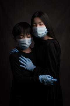 Painterly dark studio portrait of boy and girl  in black wearing blue face masks and gloves during the corona virus pandemic
