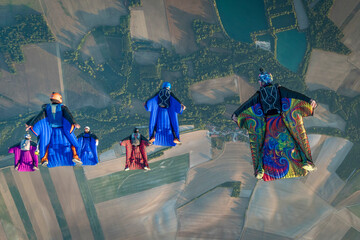 Team of wingsuit fliers glide in formation at sunset