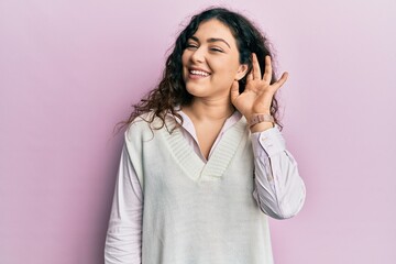 Young brunette woman with curly hair wearing casual clothes smiling with hand over ear listening an hearing to rumor or gossip. deafness concept.