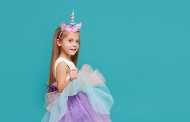Unicorn girl. Funny face. Cute child girl in elegant tulle dress and unicorn headband celebrates birthday  party on colored background © oes
