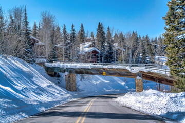 Bridge over road with view of homes and evergreens on snowy mountain in winter