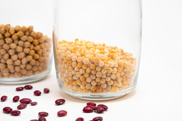 clear glass jar one quarter filled with peas and a jar of chickpeas in the background out of focus, red beans scattered partially out of focus