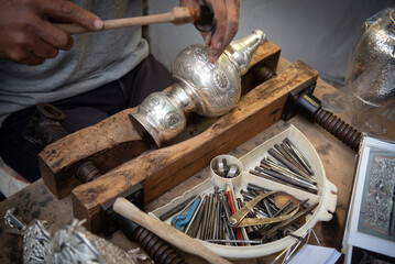 Jewellery maker working in workshop crafting homemade silver vase.