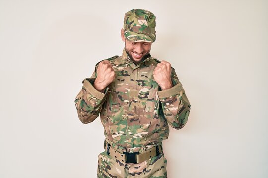 Young caucasian man wearing camouflage army uniform excited for success with arms raised and eyes closed celebrating victory smiling. winner concept.