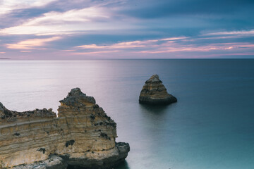 Landscape photo. Scenic rocks by the coast, still water and warm sky at dusk. Lagos, Algarve Coast, Portugal