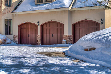 Paved driveway dusted with winter snow leading to arched garage doors of home
