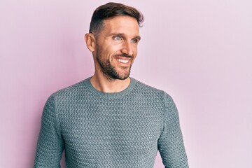 Handsome man with beard wearing casual winter sweater looking to side, relax profile pose with natural face and confident smile.