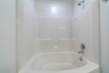 Built in bathtub with shower inside a bathroom with shiny clean white tiles