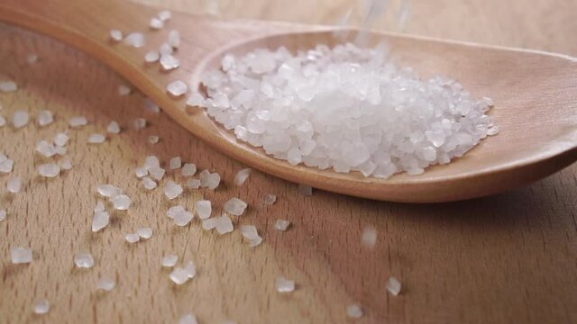 Sea salt drops close-up on a wooden spoon on a board. Slow motion. Mineral for cooking and body care