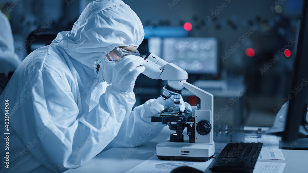 Poster research factory cleanroom: engineer / scientist wearing coverall, gloves uses microscope to inspect