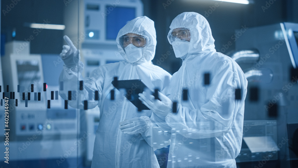 Poster factory cleanroom: engineer and scientist wearing coveralls, standing in workshop talk and use table