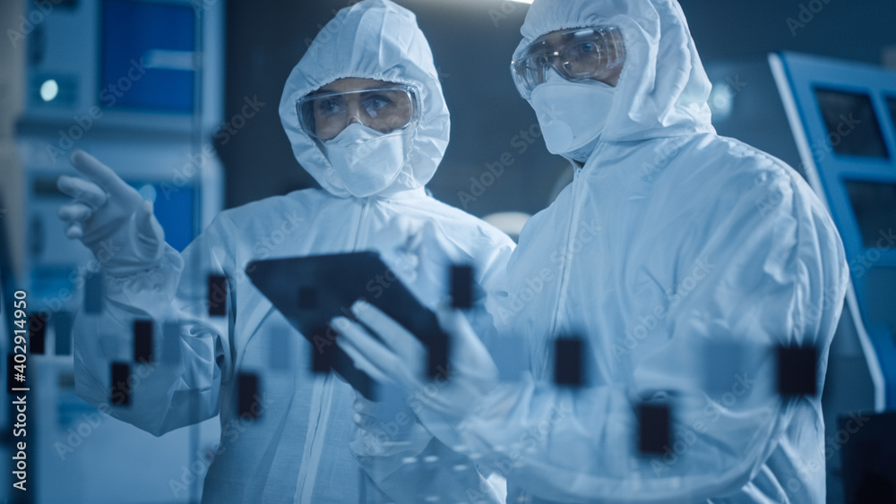 Poster factory cleanroom: engineer and scientist wearing coveralls, standing in workshop talk and use table