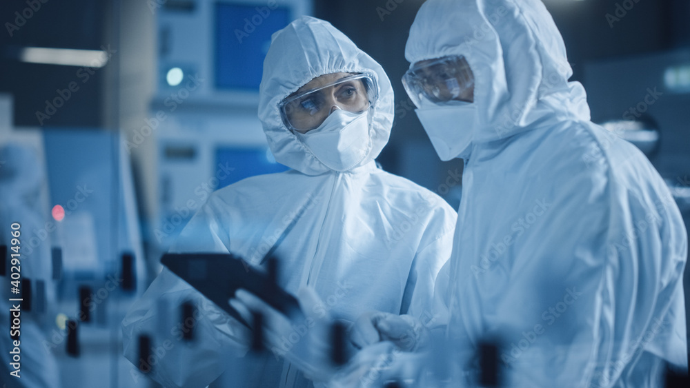 Poster factory cleanroom: engineer and scientist wearing coveralls, standing in workshop talk and use table