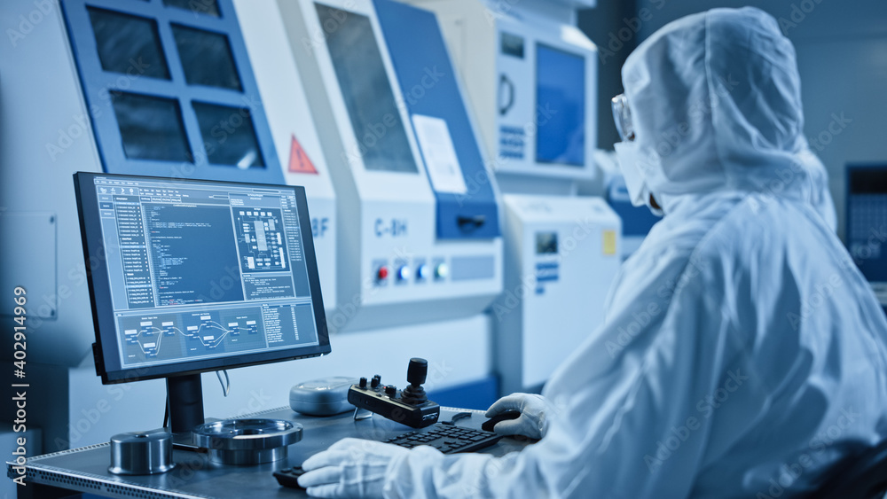Poster Factory Cleanroom: Engineer Wearing Coveralls Does System Control on a Computer, Uses Controller, Screen with CAD Software. In Background Modern CNC Machinery, Robot Arm and Electronic Equipment