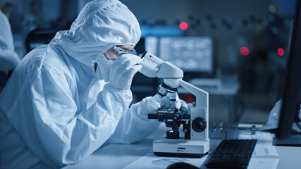Research Factory Cleanroom: Engineer / Scientist wearing Coverall, Gloves Uses Microscope to...