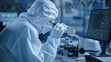 Research Factory Cleanroom: Engineer / Scientist wearing Coverall, Gloves Uses Microscope to...