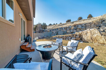 Fire pit and paved patio at sunny backyard of house with stone retaining wall