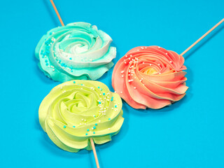 Multi-colored meringue cake on a stick on a blue background.
