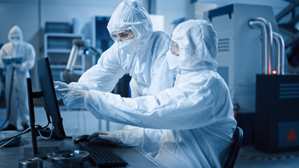 Factory Cleanroom: Engineer and Scientist Wearing Coveralls and Masks Have Discussion, Use Computer Showing Infrastructure System Control. In Background CNC Machinery, Robot Arm, Electronics Equipment