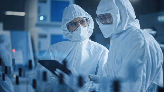 Factory Cleanroom: Engineer and Scientist Wearing Coveralls, Standing in Workshop Talk and Use Tablet Computer, Professionals Develop Technology for Modern CNC Machinery and Electronic Equipment