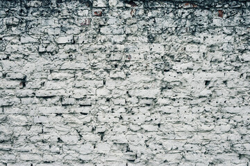 Aged white painted brick wall texture. Old textured grunge wall surface background pattern of masonry. Cracks and black stains.