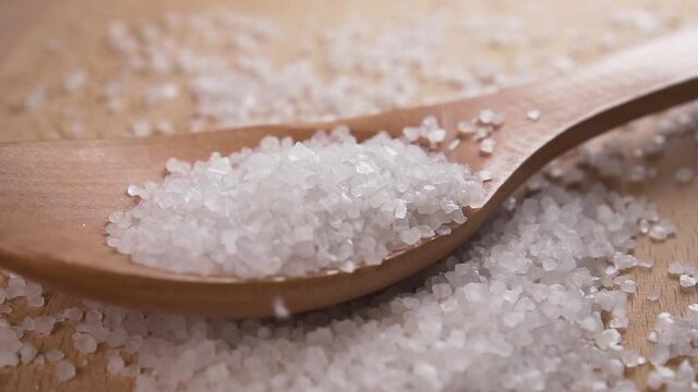 Sprinkling sea salt crystals on a wooden spoon in slow motion. Close up. Macro