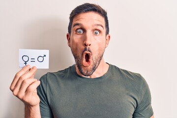 Young handsome man asking for sex discrimination holding paper with gender equality message scared...