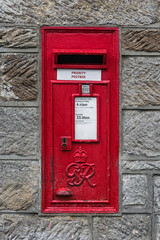 Generic old fashioned bright red vintage post box set in a stone wall.