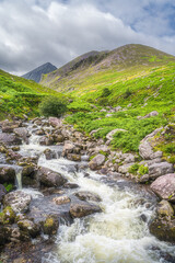 Fototapeta na wymiar Winding mountain stream or river in Cronins Yard. Green valley with Carrauntoohil in a distance, the highest mountain in Ireland, Ring of Kerry