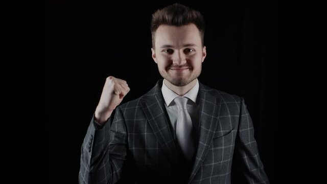 Handsome businessman wearing suit showing fist up sign with his hand isolated on black background. Happy young man wearing plaid blazer business suit gesturing. Winner. Success concept