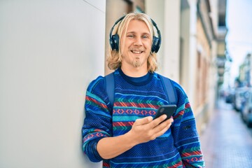Young scandinavian student man smiling happy using smartphone and headphones at the city.