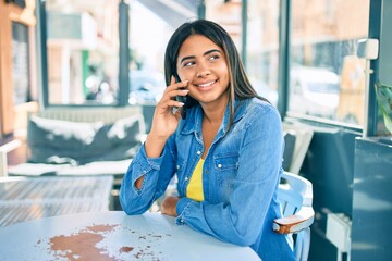 Young latin woman smiling happy talking on the smartphone at coffee shop terrace.