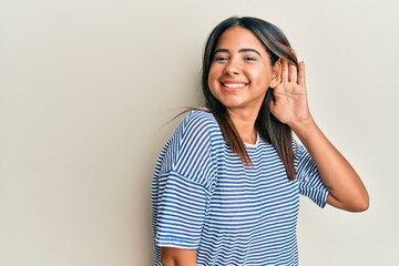 Fototapeta premium Young latin girl wearing casual clothes smiling with hand over ear listening and hearing to rumor or gossip. deafness concept.