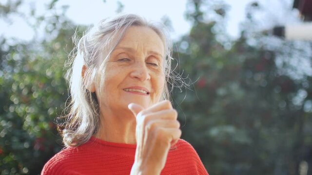 Close up face of senior woman with grey hair looking at camera while spending time outdoors during sunny day