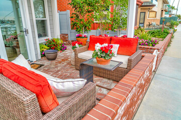 Fototapeta na wymiar Wicker bench and glass table at patio of home with colorful pillows and flowers