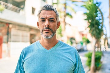 Middle age grey-haired man wearing casual clothes at street of city with serious expression on face. simple and natural looking at the camera.