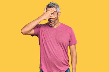 Middle age grey-haired man wearing casual clothes peeking in shock covering face and eyes with hand, looking through fingers with embarrassed expression.