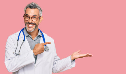 Middle age grey-haired man wearing doctor uniform and stethoscope amazed and smiling to the camera while presenting with hand and pointing with finger.