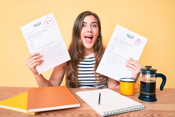 Young beautiful caucasian woman showing failed and passed exam sitting on the table celebrating crazy and amazed for success with open eyes screaming excited.