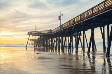 Fototapeta premium Sunset on the beach and pier. An iconic California wooden pier at 1, 370 feet long in the heart of Pismo Beach city in Central California coast.