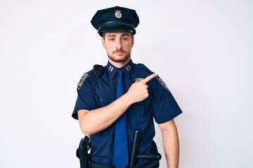 Young caucasian man wearing police uniform pointing with hand finger to the side showing advertisement, serious and calm face