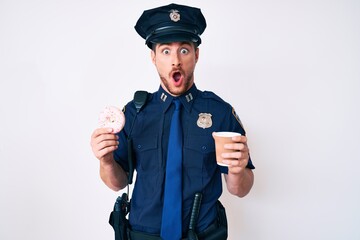 Young caucasian man wearing police uniform holding take away coffee and donut in shock face, looking skeptical and sarcastic, surprised with open mouth